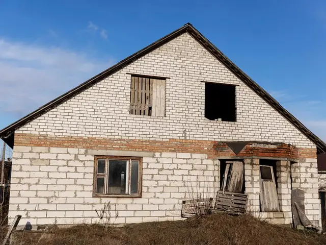Casă veche din cărămidă albă, cu ușile scoase și sprijinite lângă intrare